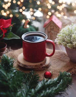 Red mug with hot beverage on wooden table with winter snow background and lights bokeh.