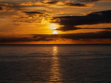 Gün batımında gökyüzü ve bulutların arasında güneş olan sakin bir deniz. Meditasyon okyanusu ve gökyüzü arka planı. Huzurlu deniz manzarası. Suyun üzerinde ufuk..