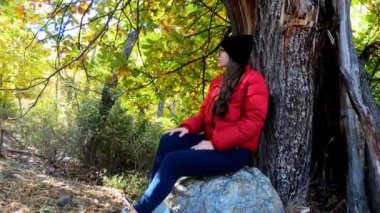 Gözlüklü ve şapkalı bir kız sonbahar parkında doğanın tadını çıkarıyor.