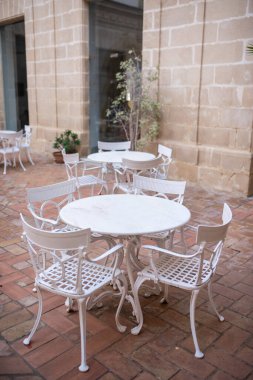 Victoria tarzı beyaz boş metal sandalyeler ve açık kafede masalar. Demir mobilyalar, eski moda kafe terası, açık terasta müşteri bekleyen restoran masaları. Kaldırımlı kafe