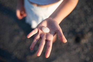 Bir çocuk nehir kıyısında bir taş tutuyor.,