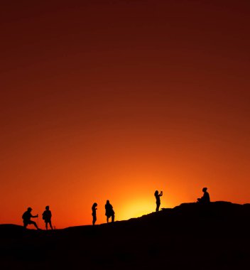 Roquetas De Mar, İspanya - 3 Haziran 2025: Siluetli insanlar kayalık arazide toplandı, sıcak renkleri ve huzurlu atmosferiyle baş döndürücü bir günbatımının tadını çıkarıyorlar.