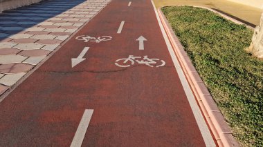 Almerya, İspanya - 25 Mayıs 2025: Bisiklet yolu yeşil çimenler ve desenli fayanslarla sınırlandırılmış dokulu kaldırım üzerinde yön sembolleri içeriyor, kentsel bisiklet güvenliğinin artırılması