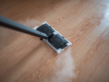 Buhar temizleme cihazı aktif olarak ahşap zemini dezenfekte ediyor. Çağdaş bir yaşam alanında etkili temizlik teknikleri gösterirken buhar yayıyor.