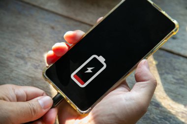 Bir adam elini kapatır ve telefonunu ahşap bir masada şarj eder.