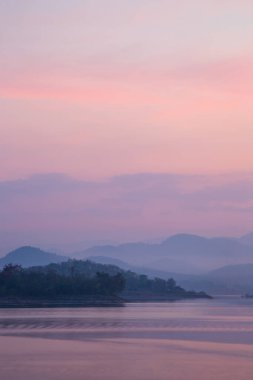 Sakin alacakaranlık renkleri, sisle kaplanmış uzak dağlarla sakin bir gölden yansıyor..