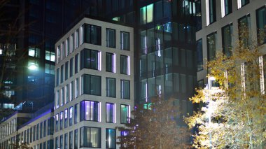 Geceleri şehirdeki modern ofis binası. Bir şirket binasının aydınlatılmış ofislerine bakın. Cam ve çelikten yapılmış çok katlı binanın penceresinde yanıp sönen ışık. Geceleri uzun pozlama