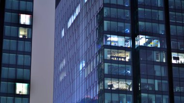 Geceleri şehirdeki modern ofis binası. Bir şirket binasının aydınlatılmış ofislerine bakın. Cam ve çelikten yapılmış çok katlı binanın penceresinde yanıp sönen ışık. Geceleri uzun pozlama
