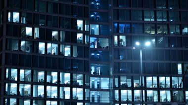 Geceleri şehirdeki modern ofis binası. Bir şirket binasının aydınlatılmış ofislerine bakın. Cam ve çelikten yapılmış çok katlı binanın penceresinde yanıp sönen ışık. Geceleri uzun pozlama