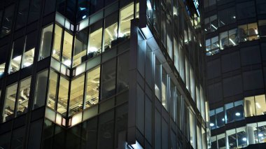 Geceleri şehirdeki modern ofis binası. Bir şirket binasının aydınlatılmış ofislerine bakın. Cam ve çelikten yapılmış çok katlı binanın penceresinde yanıp sönen ışık. Geceleri uzun pozlama