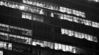 Ofis binalarının pencereleri gece aydınlandı. Cam mimari, geceleri şirket binası, iş konsepti. Siyah ve beyaz.