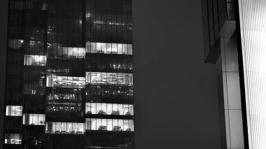 Ofis binalarının pencereleri gece aydınlandı. Cam mimari, geceleri şirket binası, iş konsepti. Siyah ve beyaz.