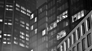 Ofis binalarının pencereleri gece aydınlandı. Cam mimari, geceleri şirket binası, iş konsepti. Siyah ve beyaz.