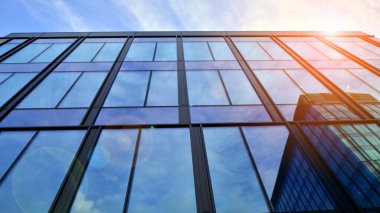 Mavi gökyüzü arka planlı cam modern bina. Düşük açı ve mimari detaylar. Şehir soyutu - güneş ışığında cam ofis binasının pencereleri.