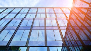 Mavi gökyüzü arka planlı cam modern bina. Düşük açı ve mimari detaylar. Şehir soyutu - güneş ışığında cam ofis binasının pencereleri.