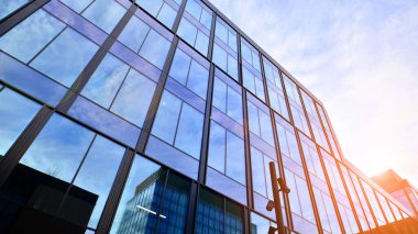 Mavi gökyüzü arka planlı cam modern bina. Düşük açı ve mimari detaylar. Şehir soyutu - güneş ışığında cam ofis binasının pencereleri.