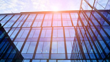 Mavi gökyüzü arka planlı cam modern bina. Düşük açı ve mimari detaylar. Şehir soyutu - güneş ışığında cam ofis binasının pencereleri.