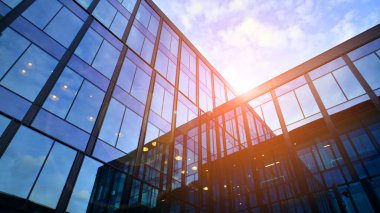 Mavi gökyüzü arka planlı cam modern bina. Düşük açı ve mimari detaylar. Şehir soyutu - güneş ışığında cam ofis binasının pencereleri.