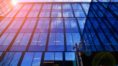 Mavi gökyüzü arka planlı cam modern bina. Düşük açı ve mimari detaylar. Şehir soyutu - güneş ışığında cam ofis binasının pencereleri.