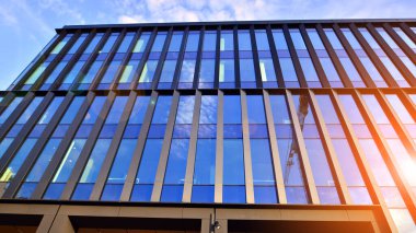 Mavi gökyüzü arka planlı cam modern bina. Düşük açı ve mimari detaylar. Şehir soyutu - güneş ışığında cam ofis binasının pencereleri.