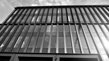 Glass modern building with sky background. Low angle view and architecture details. Urban abstract - windows of glass office building in  sunlight day. Black and white.