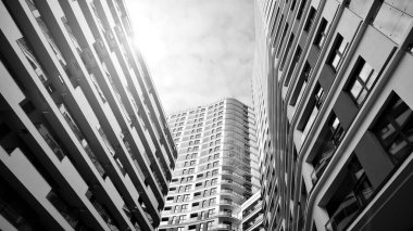 The narrow passage between modern residential buildings. Walls of high-rise apartment buildings and a narrow strip of sky between them. Modern urban living districts. Bottom view. Black and white.