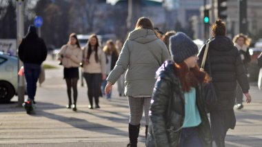 Varşova, Polonya. 8 Mart 2023. Şehir merkezindeki işlek bir caddenin arka planında parlayan güneş ışığıyla şehir kaldırımında yürüyen bir kalabalık..