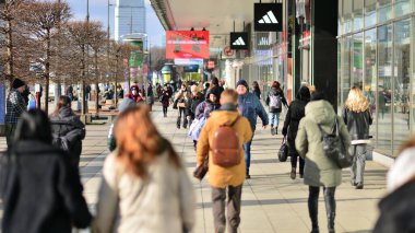 Varşova, Polonya. 8 Mart 2023. Şehir merkezindeki işlek bir caddenin arka planında parlayan güneş ışığıyla şehir kaldırımında yürüyen bir kalabalık..