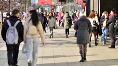 Varşova, Polonya. 8 Mart 2023. Şehir merkezindeki işlek bir caddenin arka planında parlayan güneş ışığıyla şehir kaldırımında yürüyen bir kalabalık..