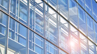 Şehir merkezindeki ticari binalara bakıyorum. Mavi gökyüzüne karşı modern ofis binası. Modern cam bir binanın pencereleri.