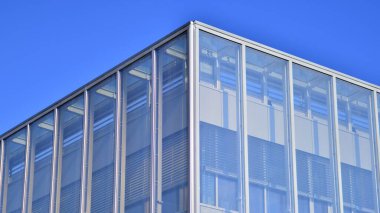 Şehirde modern bir şirket binası. Mavi gökyüzü binalara büyük cam pencerelere yansıyor. Cam cephe.