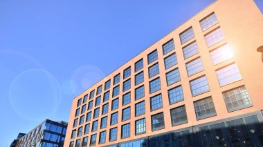 Şehirde modern bir şirket binası. Mavi gökyüzü binalara büyük cam pencerelere yansıyor. Cam cephe.