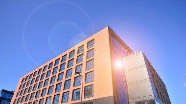 Şehirde modern bir şirket binası. Mavi gökyüzü binalara büyük cam pencerelere yansıyor. Cam cephe.