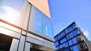 Şehirde modern bir şirket binası. Mavi gökyüzü binalara büyük cam pencerelere yansıyor. Cam cephe.