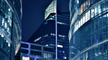 Ofis binalarının pencereleri gece aydınlandı. Cam mimari, geceleri şirket binası, iş konsepti. Mavi grafik filtresi.