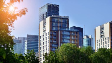 Modern şehir için ilham verici bir manzara. Cam ve metalden yapılmış binaların duvarı ağaçlara karşı. Şirket binaları ve ekolojik, mavi gökyüzü ve yeşil ağaçlı modern bina manzarası