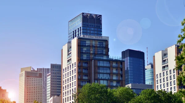 stock image Inspiring view of the modern city. The wall of the buildings of glass and metal against trees. Corporate buildings and ecological, view of modern building with blue sky and green trees