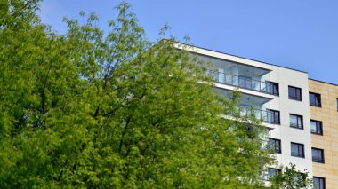 Çevre mimarisi. Yeşil ağaç ve yeni apartman. Doğanın ve modernliğin ahengi. Yeşil yerleşim bölgesinde yeni daireleri olan modern bir yerleşim yeri.. 