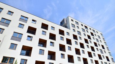 Mavi gökyüzü olan güneşli bir günde modern bir apartman. Modern bir apartmanın ön cephesi. Güneş ışığıyla kaplı cam yüzey. Ufukta yükselen güneş.