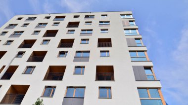 Mavi gökyüzü olan güneşli bir günde modern bir apartman. Modern bir apartmanın ön cephesi. Güneş ışığıyla kaplı cam yüzey. Ufukta yükselen güneş.