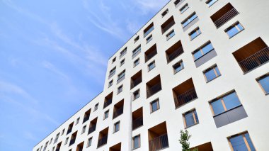 Mavi gökyüzü olan güneşli bir günde modern bir apartman. Modern bir apartmanın ön cephesi. Güneş ışığıyla kaplı cam yüzey. Ufukta yükselen güneş.