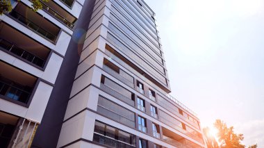 Mavi gökyüzü olan güneşli bir günde modern bir apartman. Modern bir apartmanın ön cephesi. Güneş ışığıyla kaplı cam yüzey. Ufukta yükselen güneş.