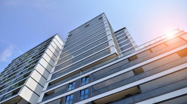 Mavi gökyüzü olan güneşli bir günde modern bir apartman. Modern bir apartmanın ön cephesi. Güneş ışığıyla kaplı cam yüzey. Ufukta yükselen güneş.