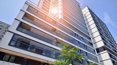 Mavi gökyüzü olan güneşli bir günde modern bir apartman. Modern bir apartmanın ön cephesi. Güneş ışığıyla kaplı cam yüzey. Ufukta yükselen güneş.