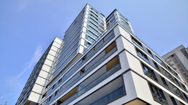 Mavi gökyüzü olan güneşli bir günde modern bir apartman. Modern bir apartmanın ön cephesi. Güneş ışığıyla kaplı cam yüzey. Ufukta yükselen güneş.