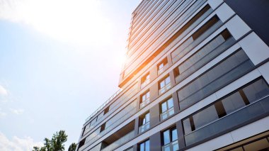 Mavi gökyüzü olan güneşli bir günde modern bir apartman. Modern bir apartmanın ön cephesi. Güneş ışığıyla kaplı cam yüzey. Ufukta yükselen güneş.