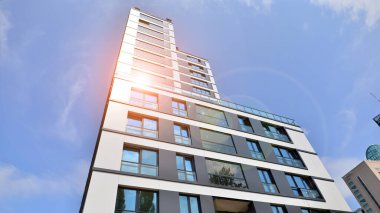 Mavi gökyüzü olan güneşli bir günde modern bir apartman. Modern bir apartmanın ön cephesi. Güneş ışığıyla kaplı cam yüzey. Ufukta yükselen güneş.