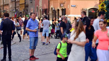 Varşova, Polonya. 29 Temmuz 2023. Sokakta yürüyen bir sürü insan. Eski bir şehir manzarasının arka planına doğru hareket eden bir kalabalık.