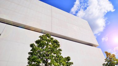 Mavi gökyüzüne karşı modern beyaz beton bina duvarları. Çevre mimarisi. Yeşil ağaçlar ve beton ofis binası. Doğanın ve modernliğin ahengi.