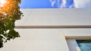 Mavi gökyüzüne karşı modern beyaz beton bina duvarları. Çevre mimarisi. Yeşil ağaçlar ve beton ofis binası. Doğanın ve modernliğin ahengi.